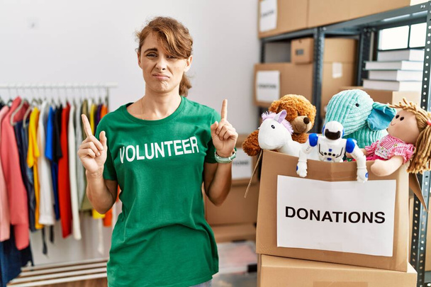 Beautiful caucasian woman wearing volunteer t shirt at donations stand pointing up looking sad and upset, indicating direction with fingers, unhappy and depressed.  - Photo, Image