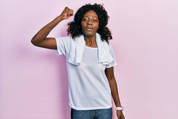 Young african american woman wearing sportswear and towel angry and mad raising fist frustrated and furious while shouting with anger. rage and aggressive concept.  - Foto, Imagen