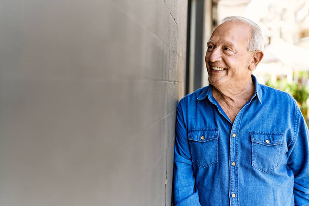 Homem sênior com cabelos grisalhos em pé feliz ao ar livre em um dia ensolarado. Sorrindo feliz aos 70 anos para a aposentadoria. - Foto, Imagem