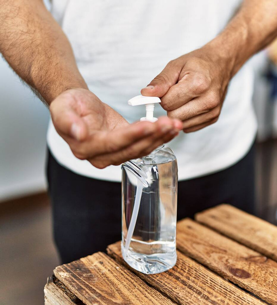 Jovem hispânico homem cliente limpeza mãos usando gel desinfetante na loja de roupas - Foto, Imagem