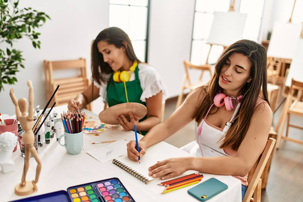 Deux élèves de peinture latine souriant peinture heureuse assis sur la table à l'école d'art. - Photo, image