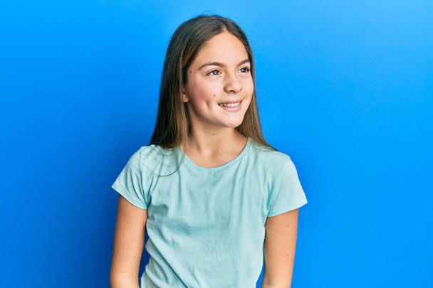 Beautiful brunette little girl wearing casual white t shirt looking away to side with smile on face, natural expression. laughing confident.  - Φωτογραφία, εικόνα
