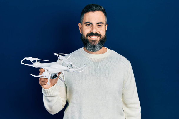 Νεαρός Ισπανόφωνος κρατώντας drone φαίνεται θετική και ευτυχισμένη στέκεται και χαμογελά με αυτοπεποίθηση χαμόγελο δείχνει τα δόντια  - Φωτογραφία, εικόνα