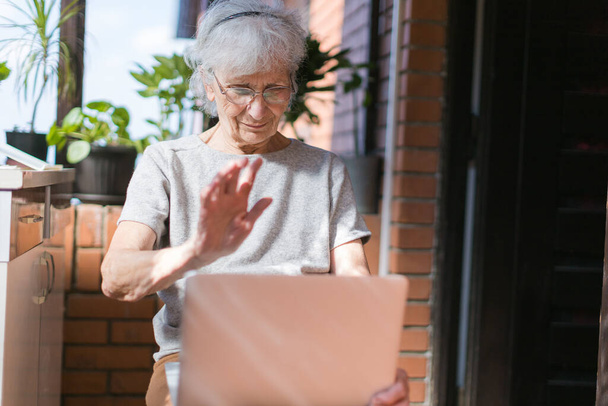 old woman on her terrace chatting via laptop - Foto, Imagen