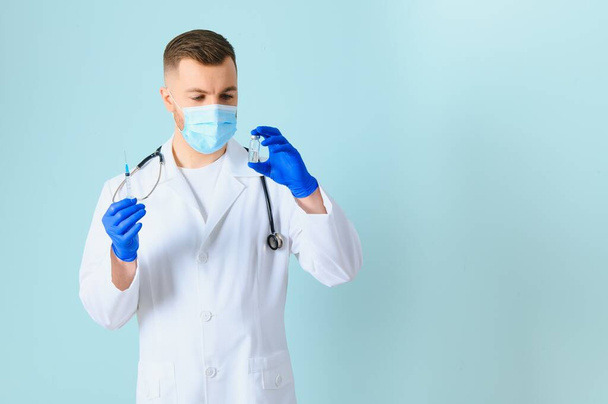 Young male doctor holding syringe with covid vaccine, ready to do coronavirus vaccination, isolated on blue background - Zdjęcie, obraz