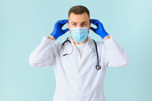 Male doctor in medical mask on color background - 写真・画像