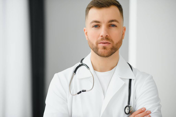 Portrait of smiling doctor looking at camera with arms crossed in medical office - Foto, Bild
