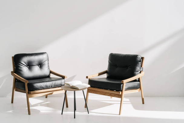 Dos sillones de cuero minimalistas de pie cerca de la mesa de centro en la oficina de lujo o apartamento con estilo brillante. Libro abierto, agenda o planificador en la sala de reuniones del centro de negocios - Foto, Imagen