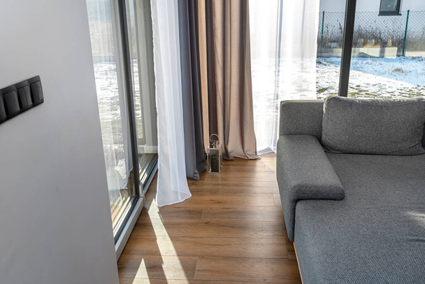 Geniş verandalı ve çift perdeli modern ve basit oturma odası görünür gri bir kanepe ve küçük bir fener.. - Fotoğraf, Görsel