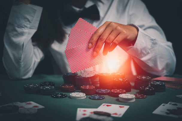 Asyalı kadın satıcı ya da krupiye, elinde iki iskambil kâğıdı olan bir kadının arka planındaki kumarhanede poker kartları karıştırıyor. Kumarhane, poker, poker konsepti - Fotoğraf, Görsel