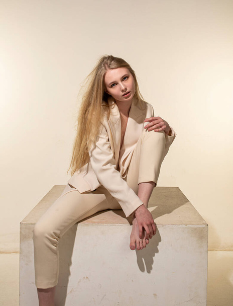 Sitting young woman with blonde hair isolated on beige - Foto, Imagen