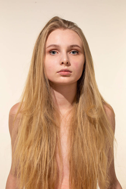 Giovane donna bianca con lunghi capelli biondi isolati su ritratto beige - Foto, immagini
