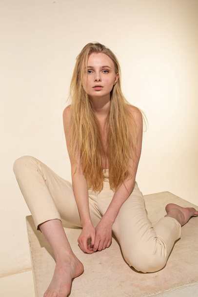 White young woman with blonde hair isolated on beige sitting - Фото, зображення