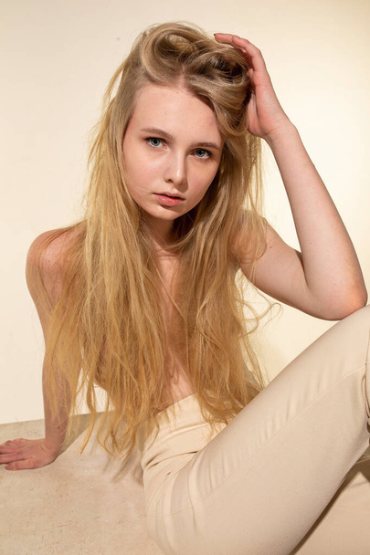 European young woman with blonde hair isolated on beige holding her hair by hand - Фото, зображення