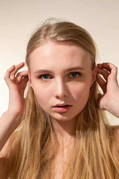 Portrait of young woman with blonde hair isolated on beige with hands near the face - Photo, Image