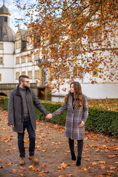 White young european married couple with building behind walking in autumn park - Foto, afbeelding