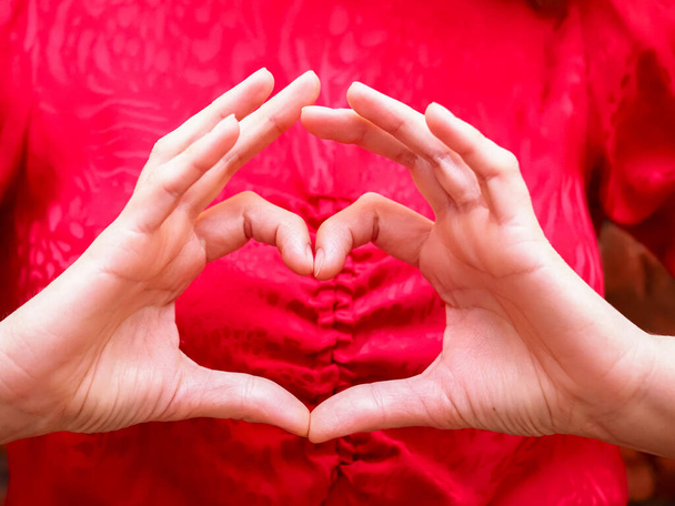 Ένα κορίτσι με κόκκινο φόρεμα δείχνει ένα σχήμα καρδιάς με το δάχτυλό της. - Φωτογραφία, εικόνα