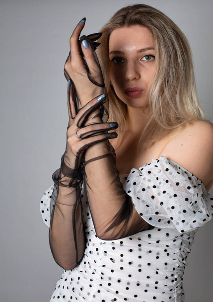 European woman with blonde hair and white skin isolated on dark grey in white dress with black dots - Fotó, kép