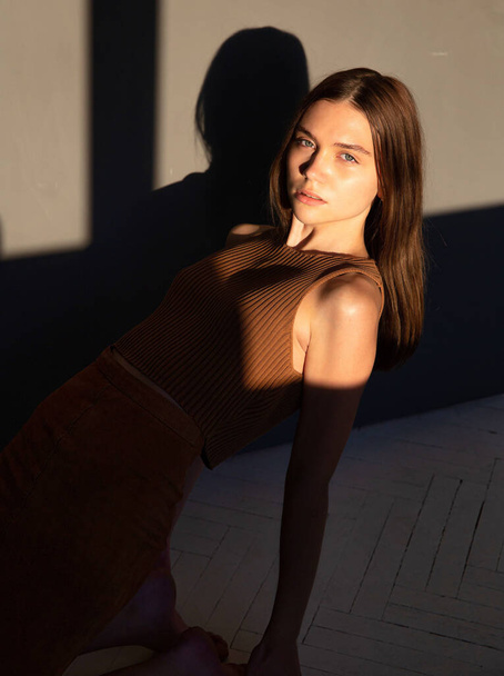 In sunset light woman with dark hair and white skin isolated on dark beige with shadows - Foto, afbeelding