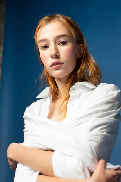 Portrait of girl with red hair and white skin isolated on blue with folded arms - Foto, afbeelding