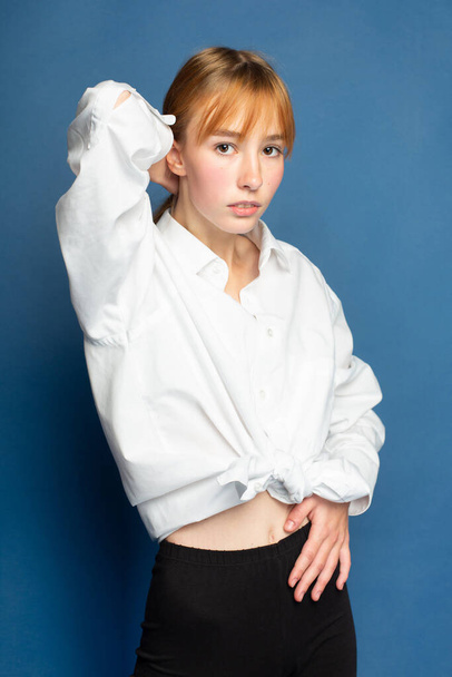 Girl with red hair and white skin isolated on blue in white blouse - 写真・画像