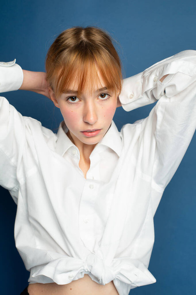 Portrait girl with red hair and white skin isolated on blue in white shirt - Photo, Image
