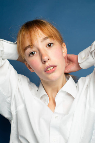 Portrait girl with red hair and white skin isolated on blue in white shirt - Fotó, kép