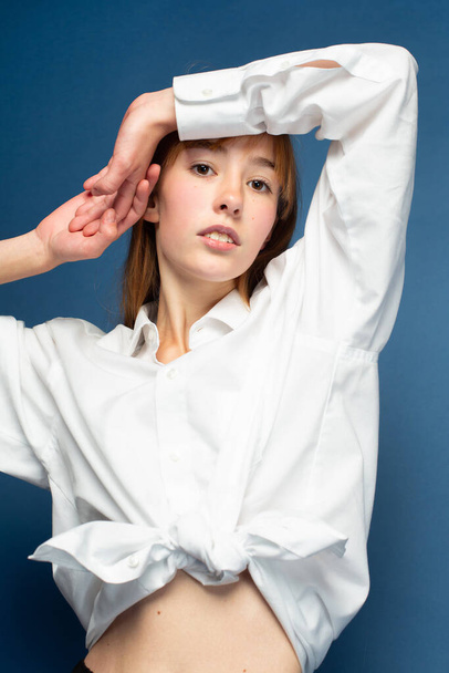 Girl with red hair and white skin isolated on blue in white shirt - 写真・画像