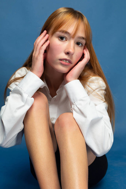 Young girl with red hair and white skin isolated on blue with hands near her face - Foto, Bild