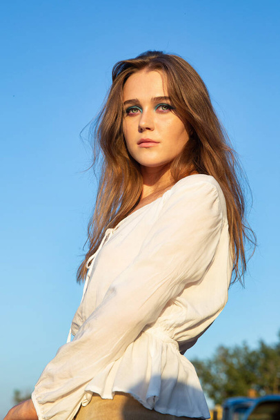 Serious young woman with white skin with sky behind in sunset light - Foto, imagen
