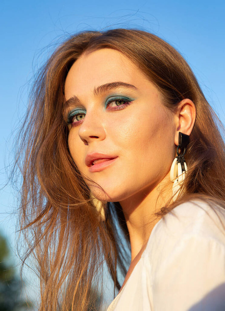 Portrait of young woman with white skin with sky behind with blue eyeliner - Foto, afbeelding