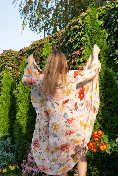 Turned back young woman with white skin with greenery behind in floral dress - Foto, immagini