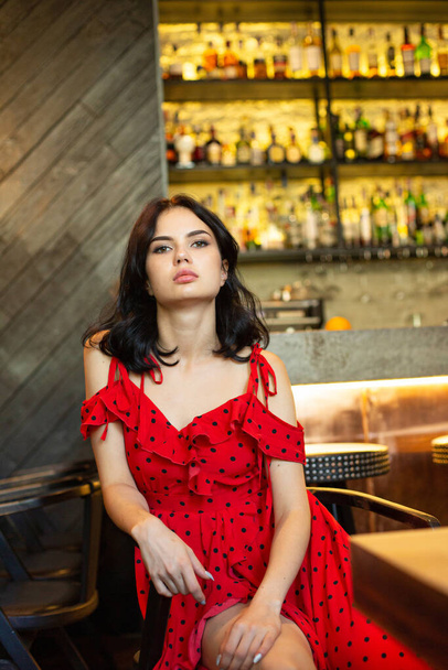 Young dark haired woman with white skin in bar in red dress - Foto, Bild