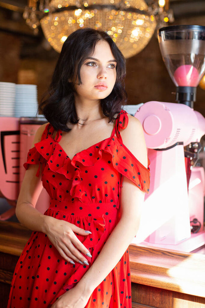 Young dark haired woman with white skin in restaurant in red dotted dress - Fotoğraf, Görsel