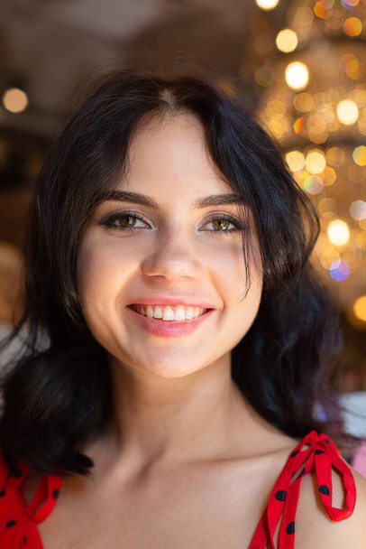 Portrait of smiling young dark haired woman with white skin with lights behind with plump lips and expressive eyes - Photo, Image