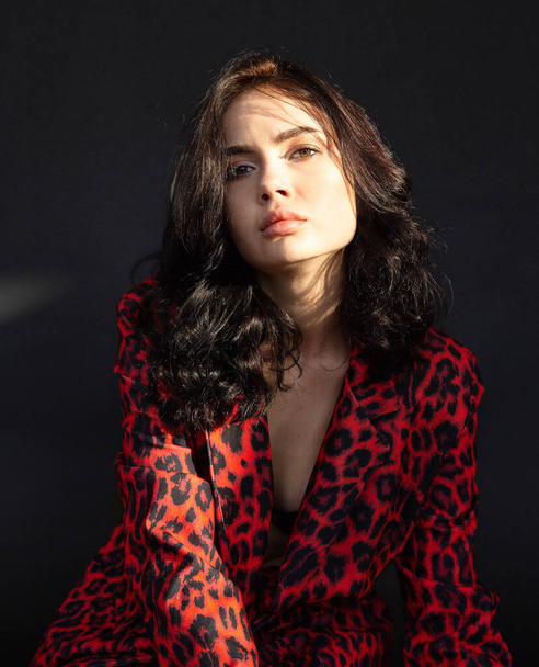 Portrait of young dark haired woman with white skin on dark background in leopard print clothes - Foto, afbeelding