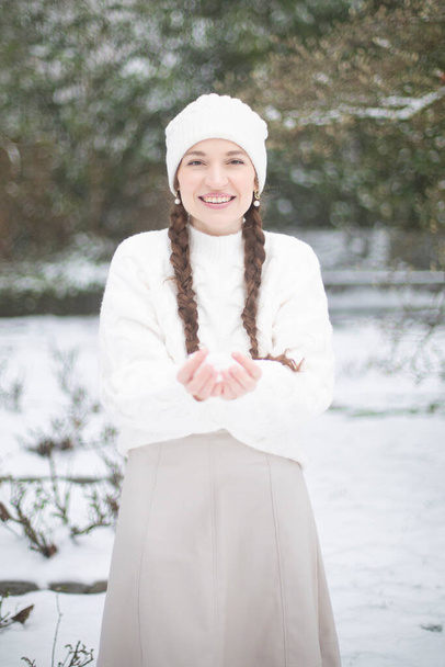 Cute young woman with white skin and long pigtails in winter park with snow - Фото, изображение
