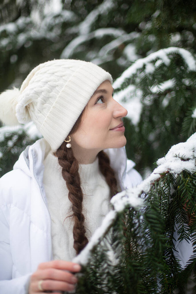 Portrait of young woman with white skin and long pigtails near spruce covered with snow - Foto, imagen