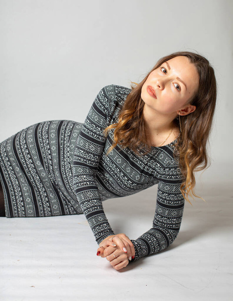 Lying young woman in warm striped dress isolated on light grey - Photo, image