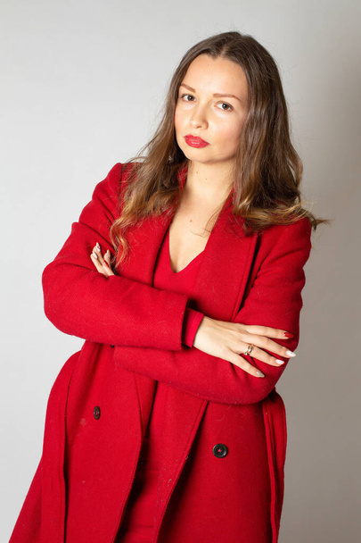 魅力的な若いですヨーロッパの女性で赤コートで孤立ライトグレーで折り畳まれた腕 - 写真・画像