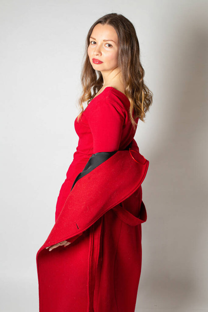 Attractive young european woman standing isolated on light grey in red coat - Photo, Image