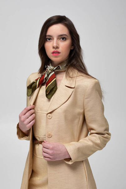 European woman with dark hair in beige suit with bright silk scarf isolated on light grey - Фото, изображение