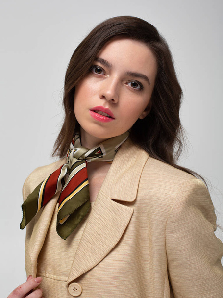 Portrait of european woman with dark hair in beige suit with bright silk scarf isolated on light grey - Foto, immagini