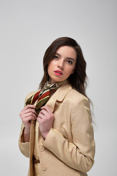 Portrait of european woman with dark hair in beige suit with bright silk scarf isolated on light grey - Fotó, kép