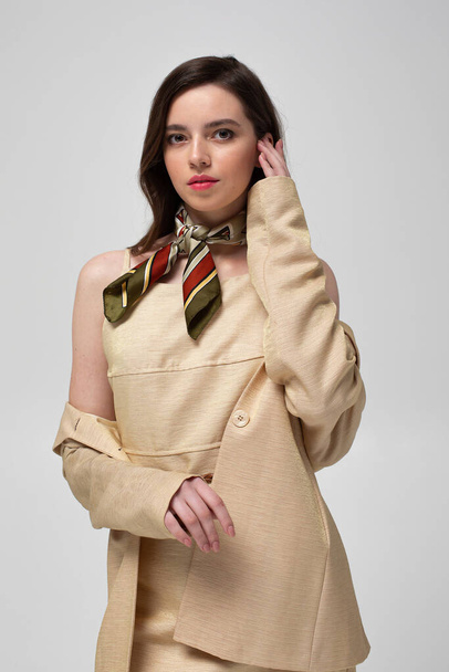 Pretty european woman with dark hair in beige suit with bright silk scarf isolated on light grey - Fotó, kép