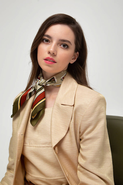 Portrait of pretty european woman with dark hair in beige suit with bright silk scarf isolated on light grey - Foto, imagen