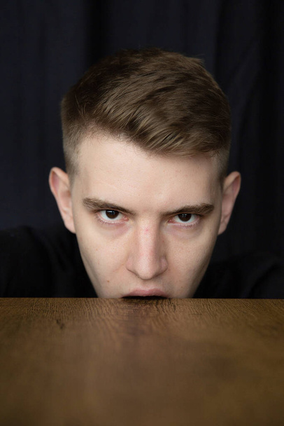 Portrait of young blond man isolated on black biting the table - Fotó, kép