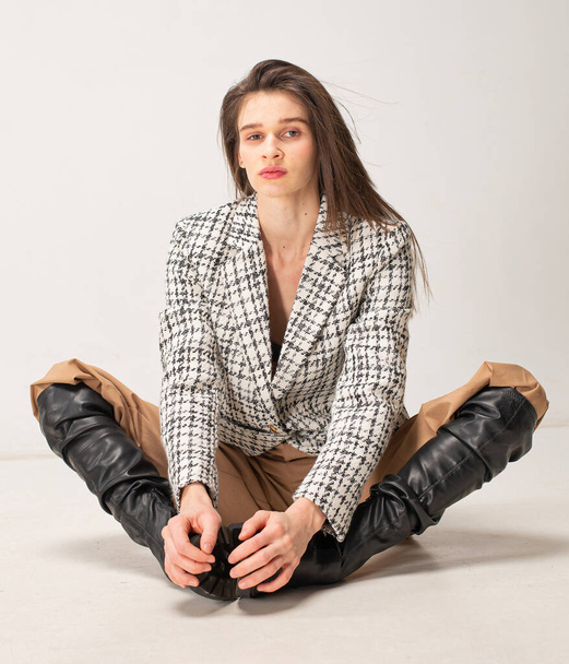 Young slim woman with dark hair isolated on light beige sitting on the floor with legs apart - Foto, Imagen