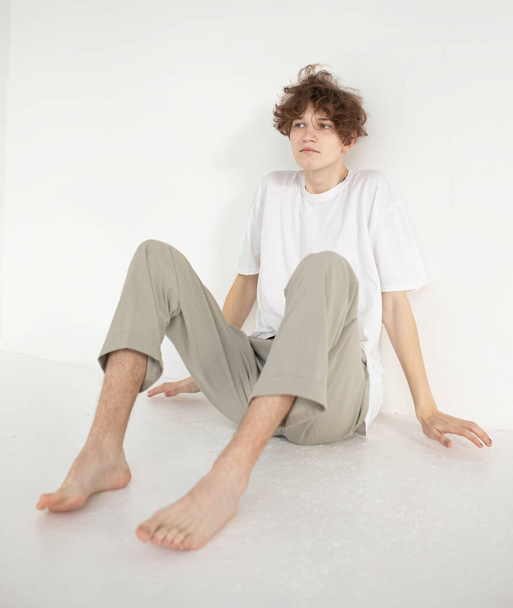 Barefoot attractive young european man isolated on beige sitting on the floor - Φωτογραφία, εικόνα