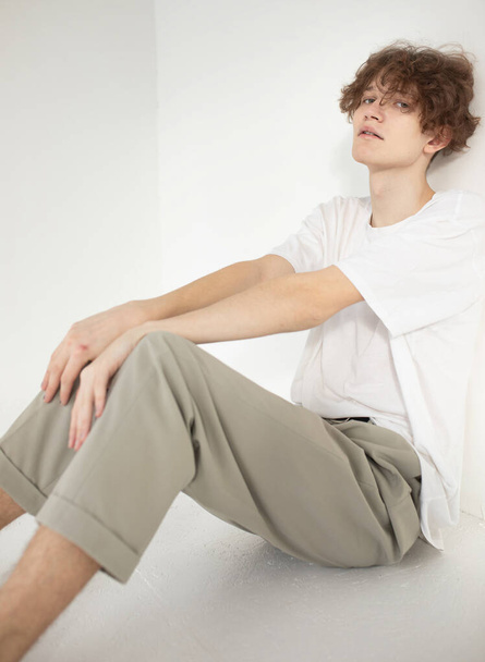 Attractive young european man isolated on beige sitting on the floor in white shirt - Valokuva, kuva